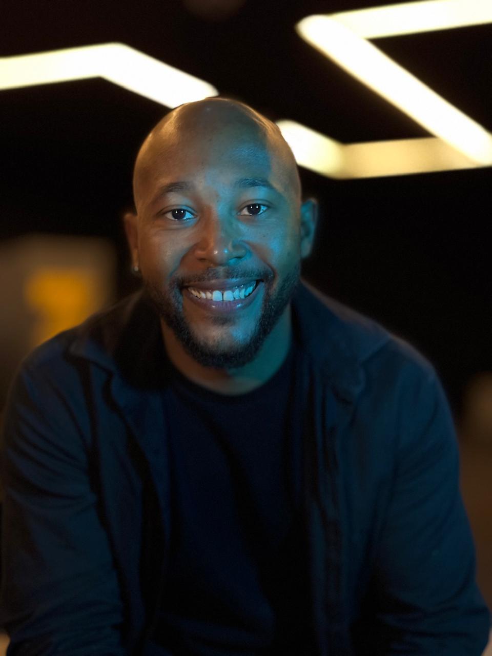 Professor Lucas Sampaio sorrindo em um ambiente com iluminação dourada e azul